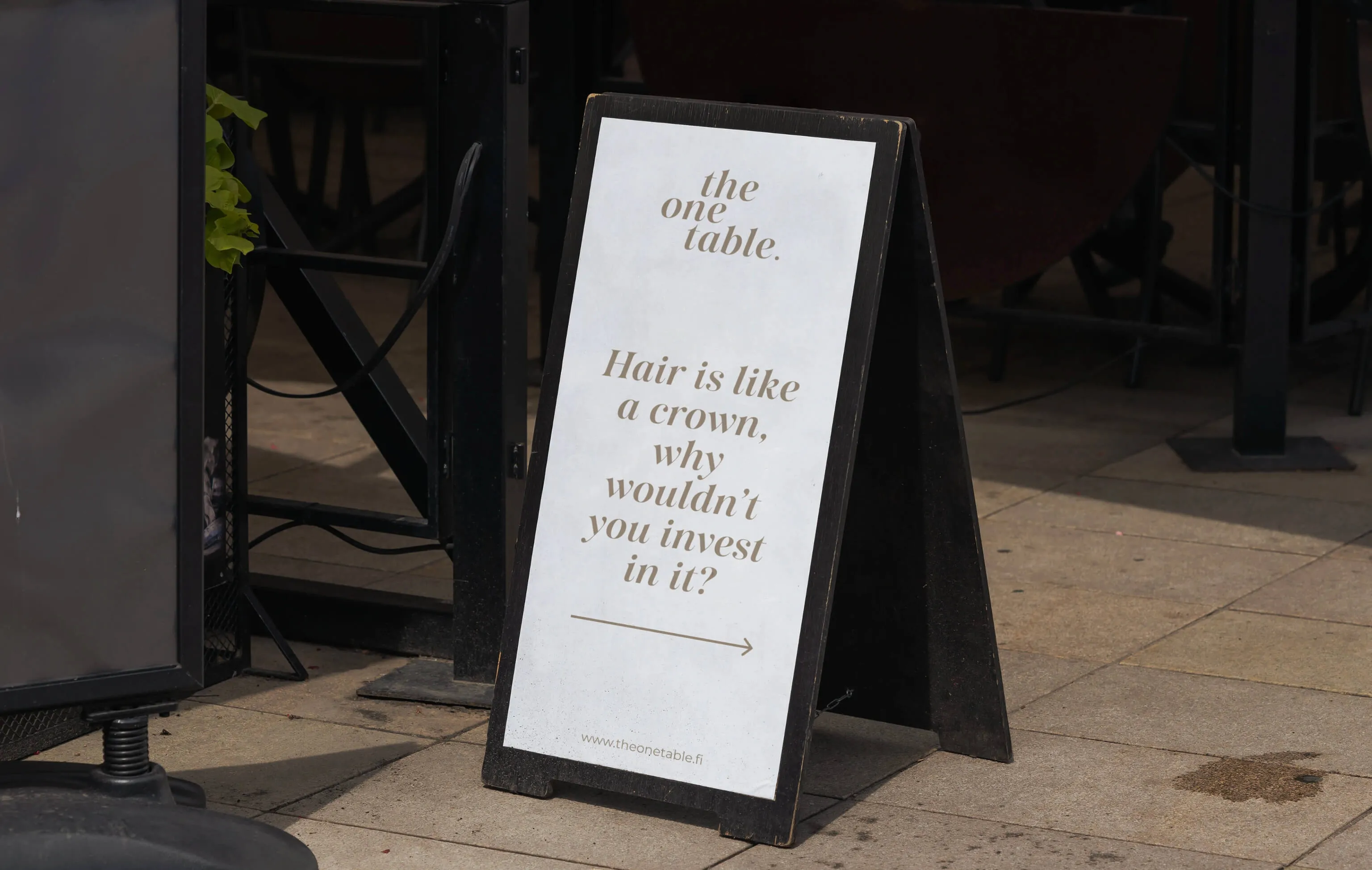 Black sandwich board sign on a sidewalk with text promoting hair care investment and an arrow pointing right.