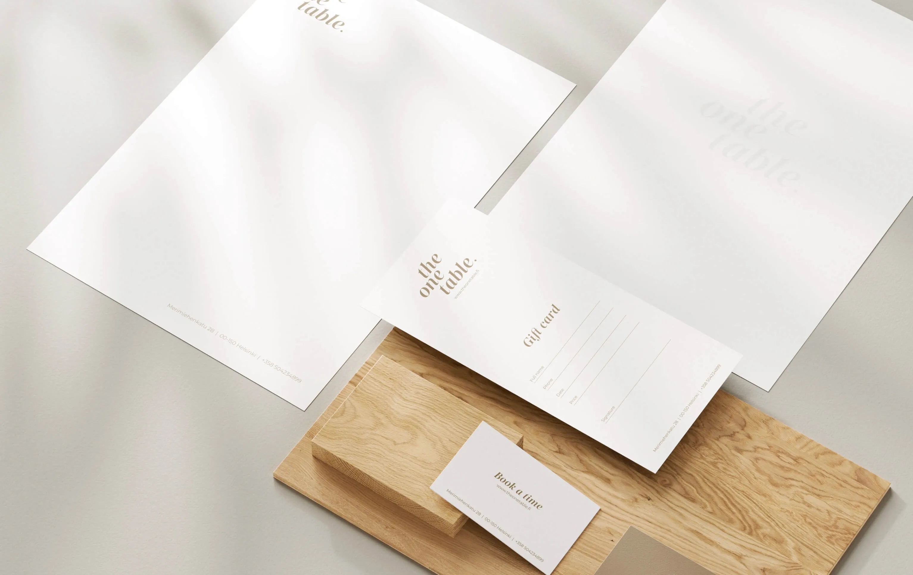 Minimalist branded stationery including letterheads, a gift card, and a business card on a wooden tray with soft shadows.