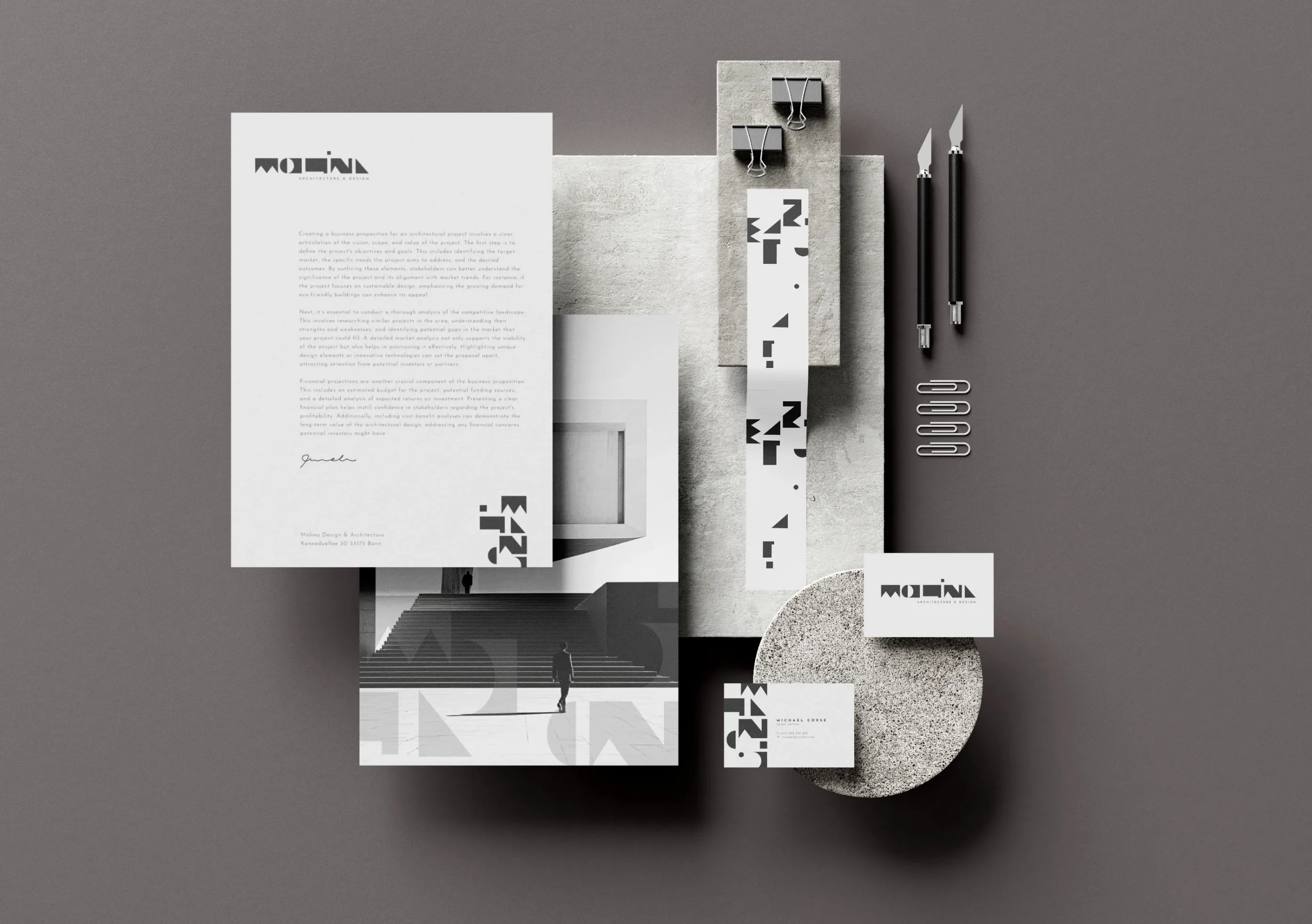 Minimalist architect branding set with letterhead, business cards, pencils, and clips arranged on gray textured surfaces.