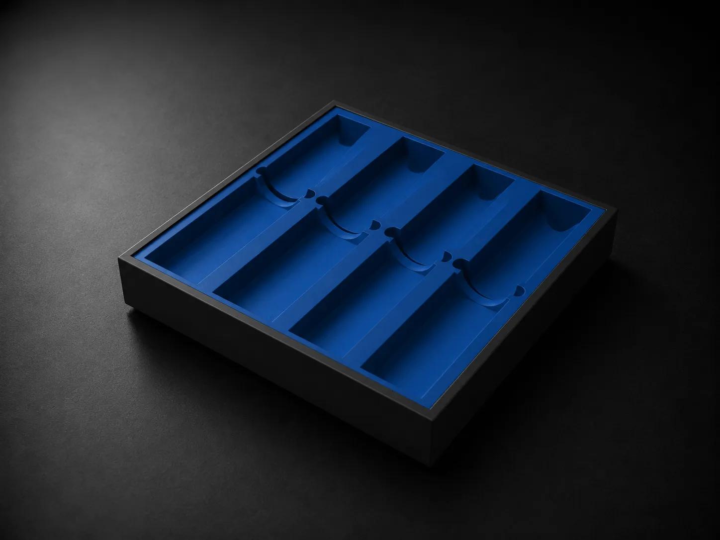 Black rectangular tray with four long blue compartments on a black surface.
