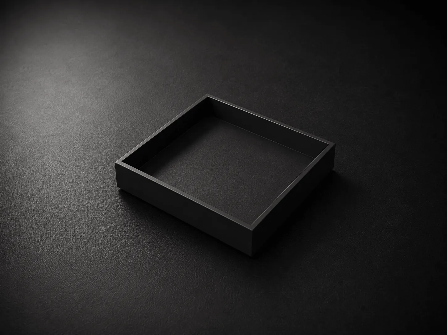 Empty black square tray on a dark textured surface with subtle lighting.