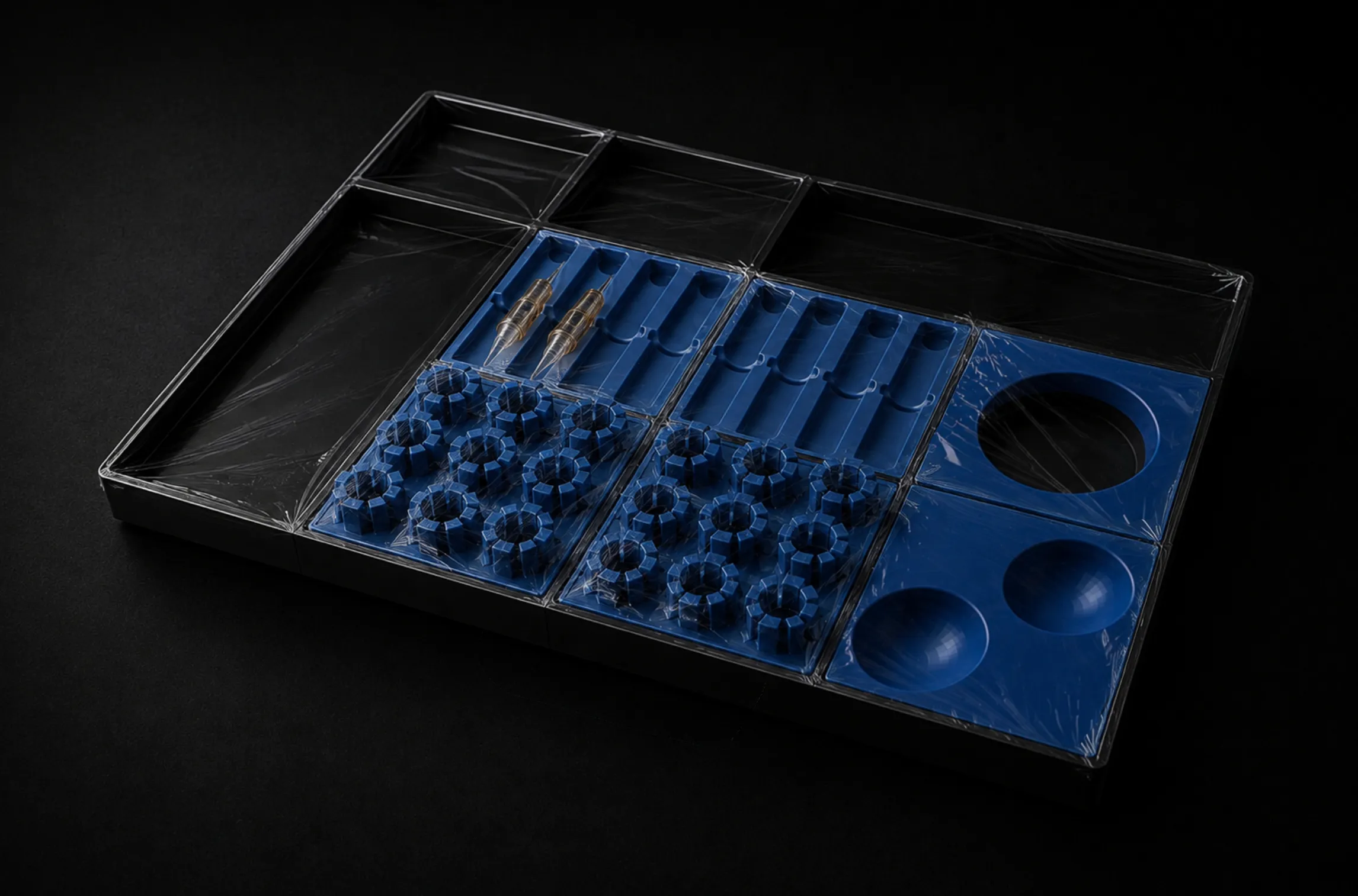 Blue plastic organizer tray with compartments covered in clear plastic wrap on a dark surface.