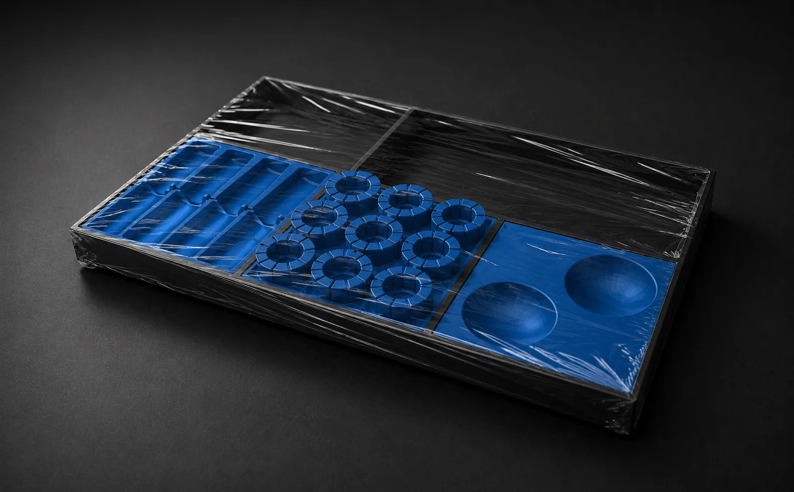 Blue silicone molds in a black tray wrapped in plastic on a dark surface.