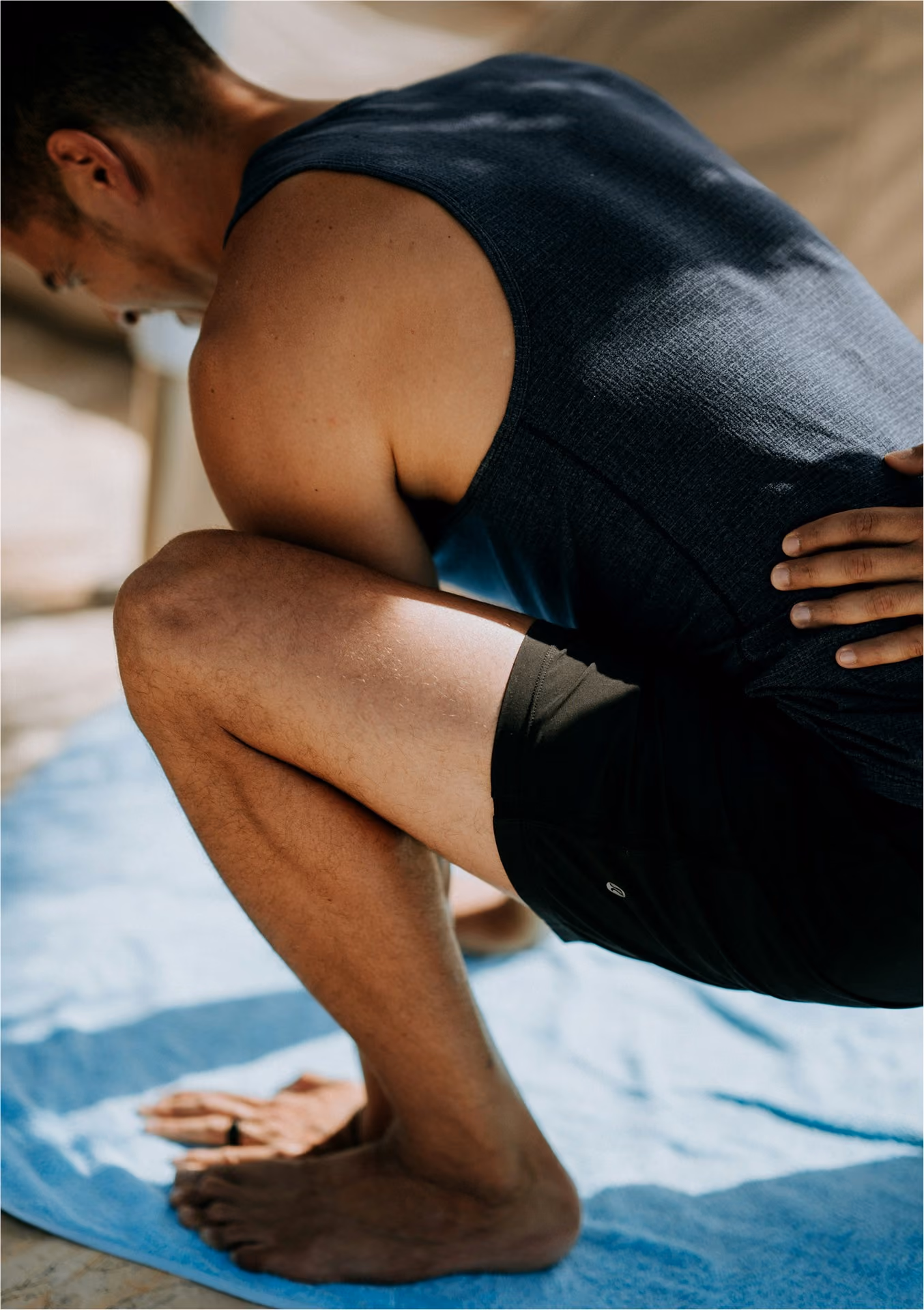 A man in a grey singlet crouching on a mat holding his lower back