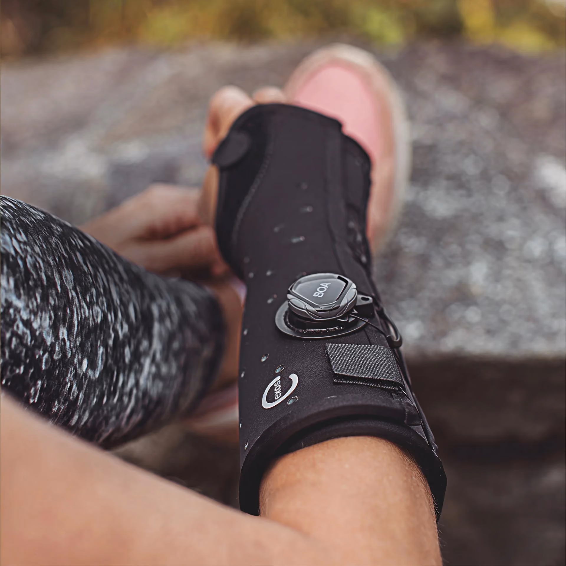 Person fitting a black Exos ankle brace with a BOA dial onto their lower leg