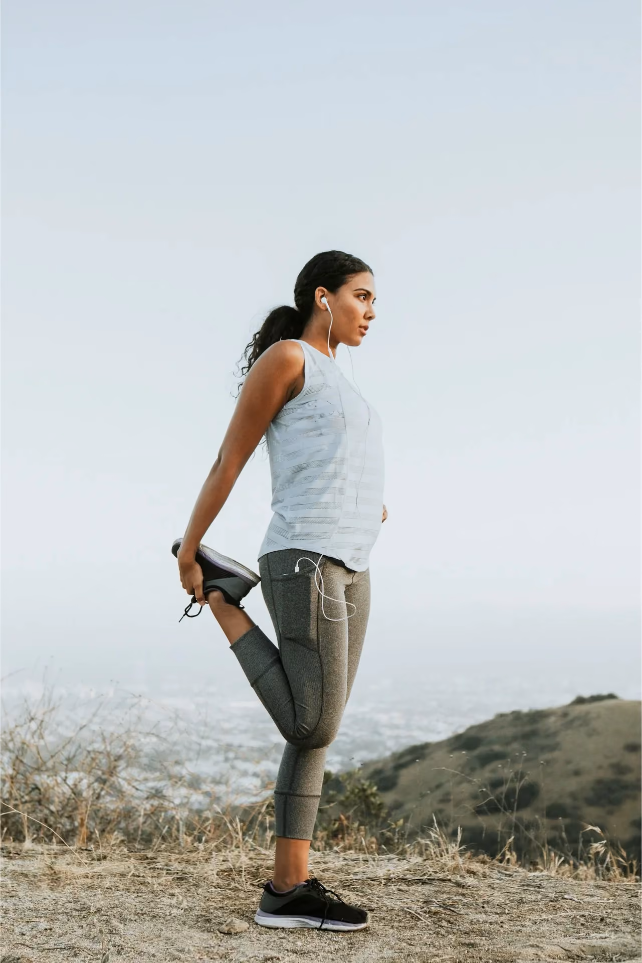 Woman stretching her quadriceps after a run on a hillside trail