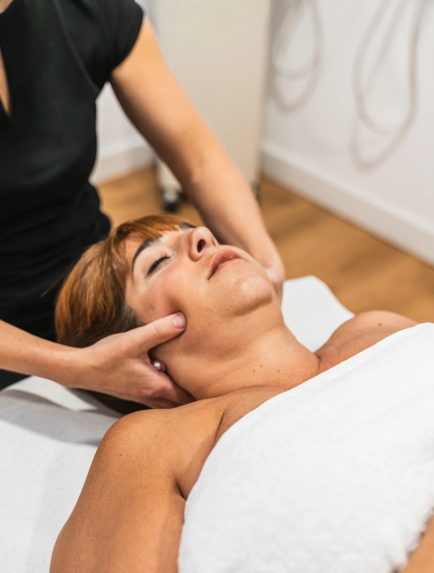 Physiotherapist applying gentle pressure around a woman's jaw while she lies on a treatment table.