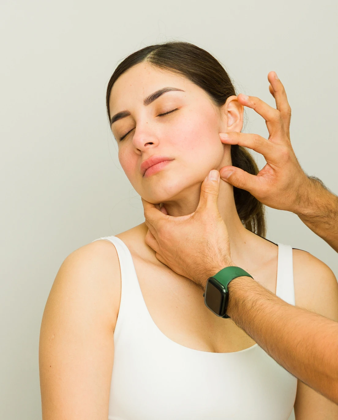 Physiotherapist providing hands-on care around a seated woman's jaw and neck.