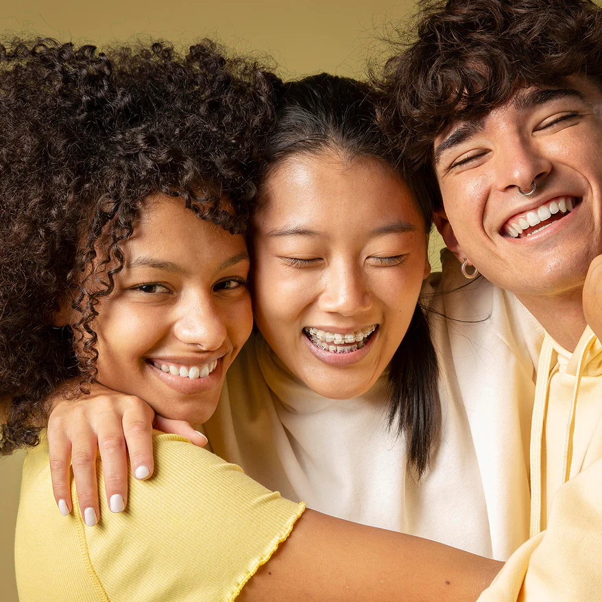 Three smiling young adults embracing, showing friendship and happiness.