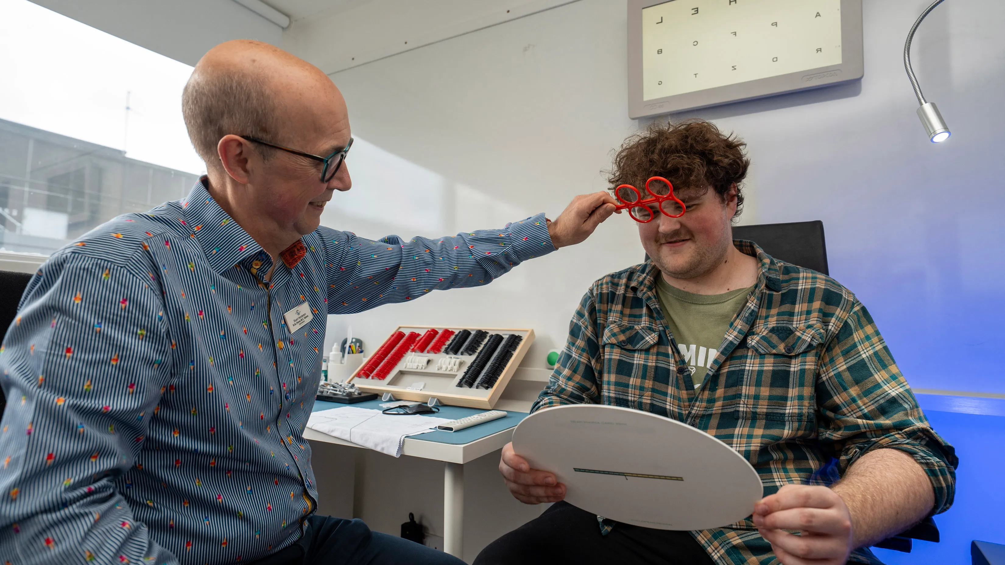 Optician adjusting red trial frames for patient during eye exam