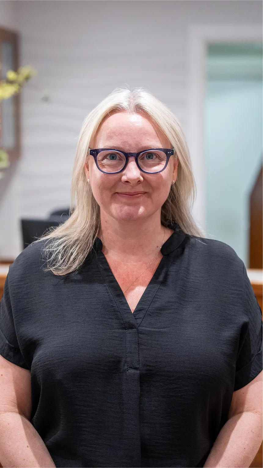 Middle-aged woman with blonde hair and blue glasses smiling