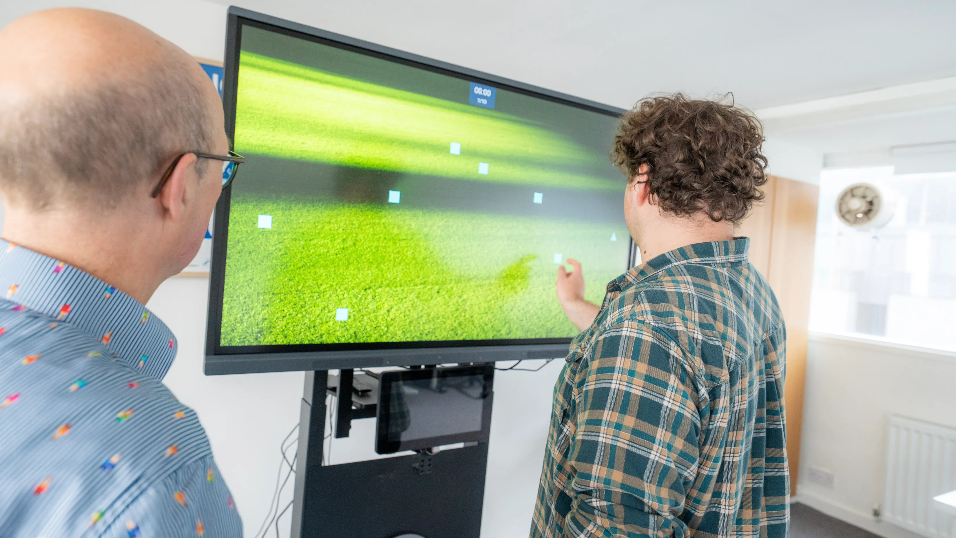 Two people examining green data visualization on large monitor