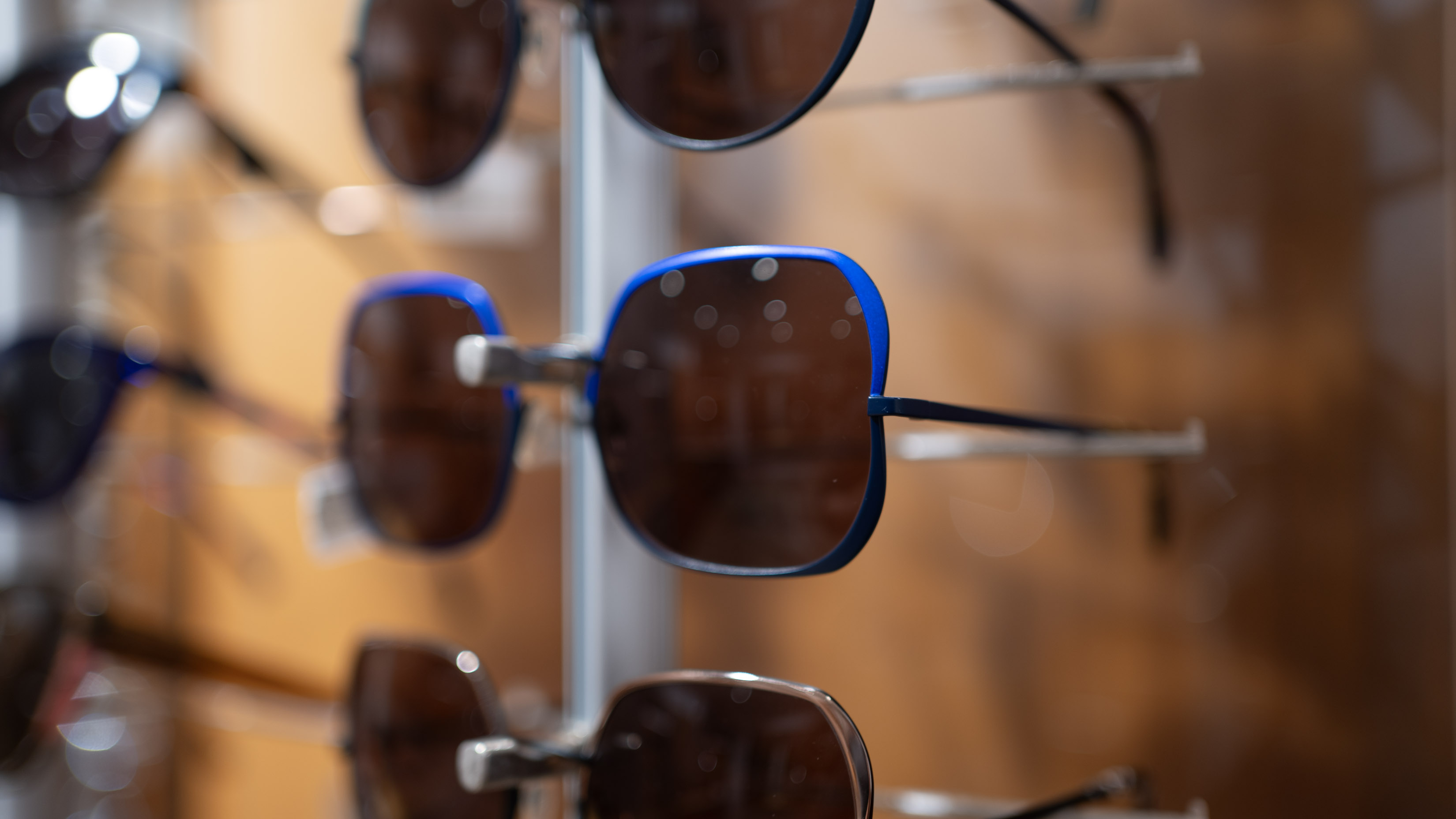 Blue-rimmed sunglasses hanging on display rack in optical store