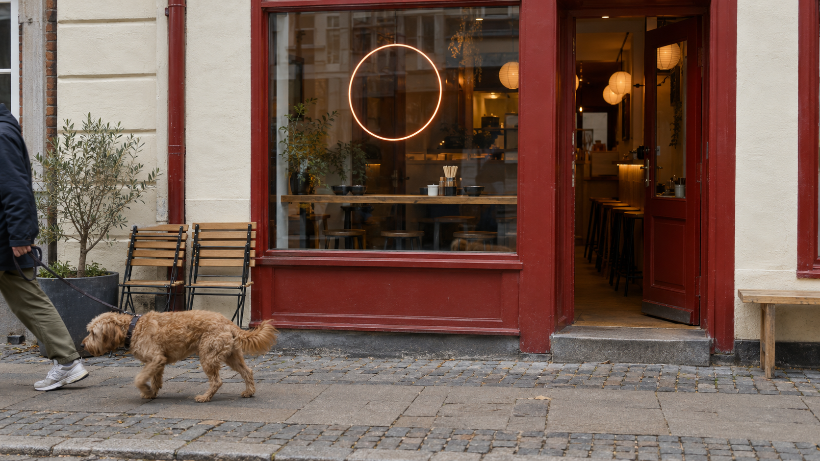 The red-framed exterior of a small Copenhagen restaurant with a dog and its owner walking past