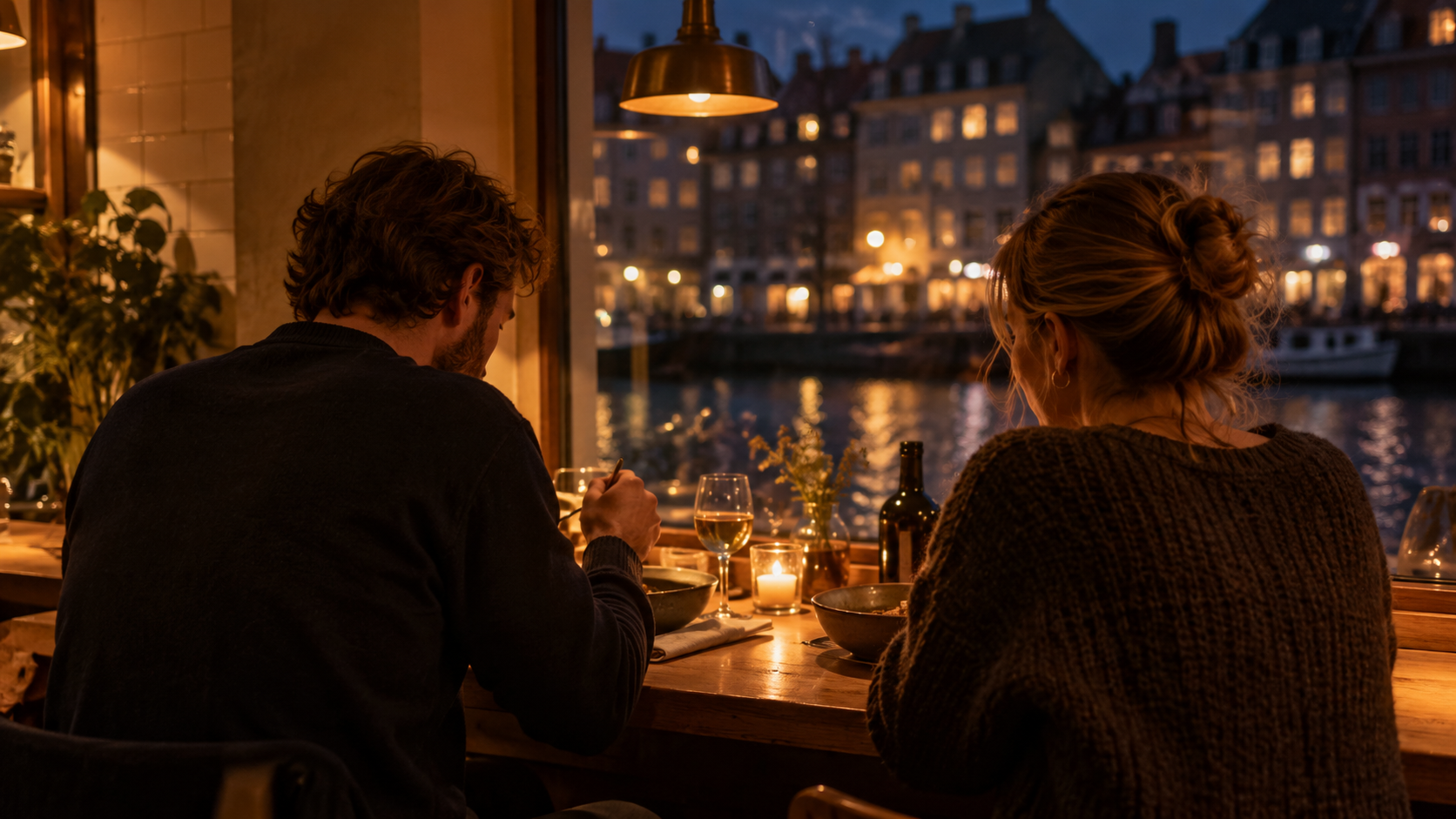 Two people seated side by side at a narrow wooden counter in a warm, dimly lit Copenhagen restaurant in the evening
