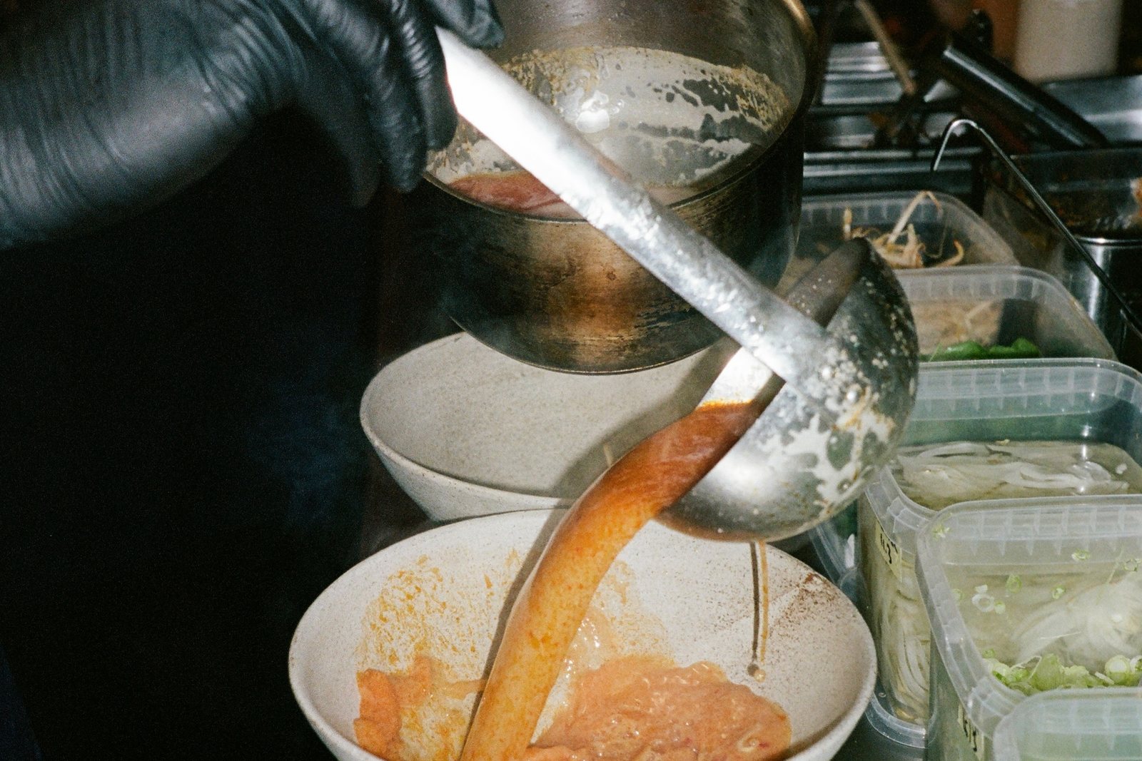 A cook ladling broth into a bowl at Slurp's pass, ready for the next table