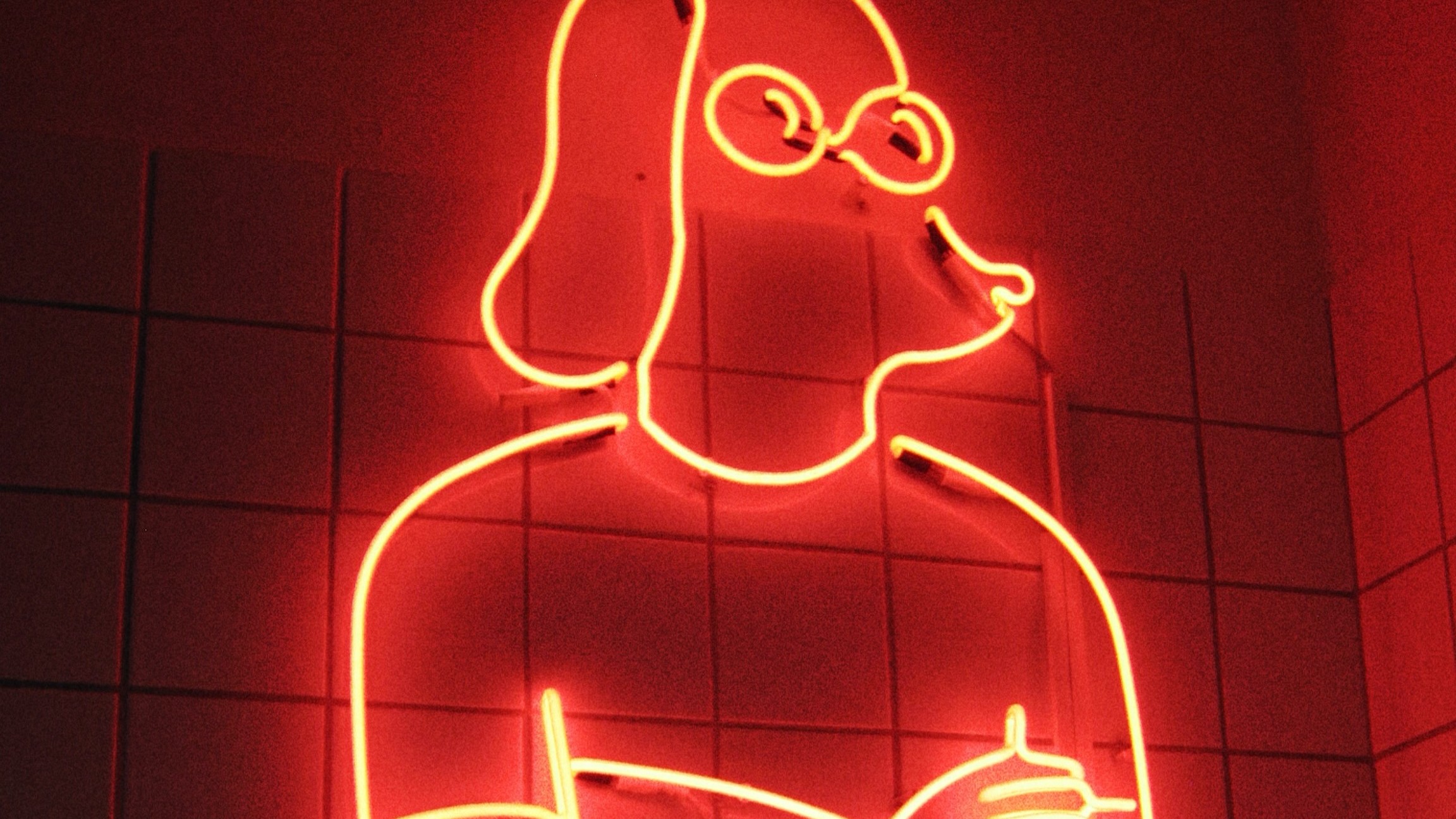 Red neon outline of a dog in round glasses with folded arms glowing against a tiled wall