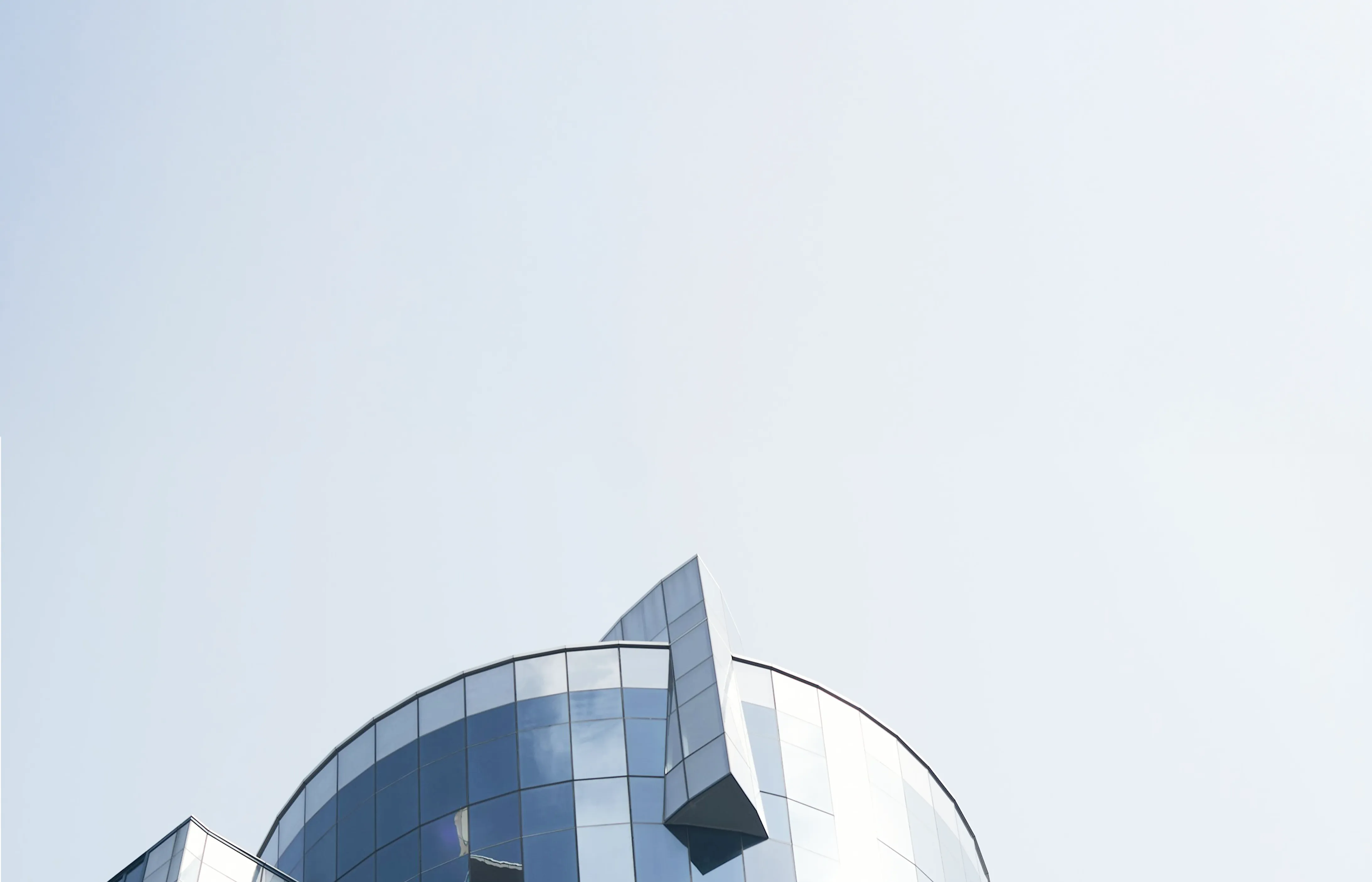 Top section of a modern cylindrical glass building with a unique angular extension against a clear sky.