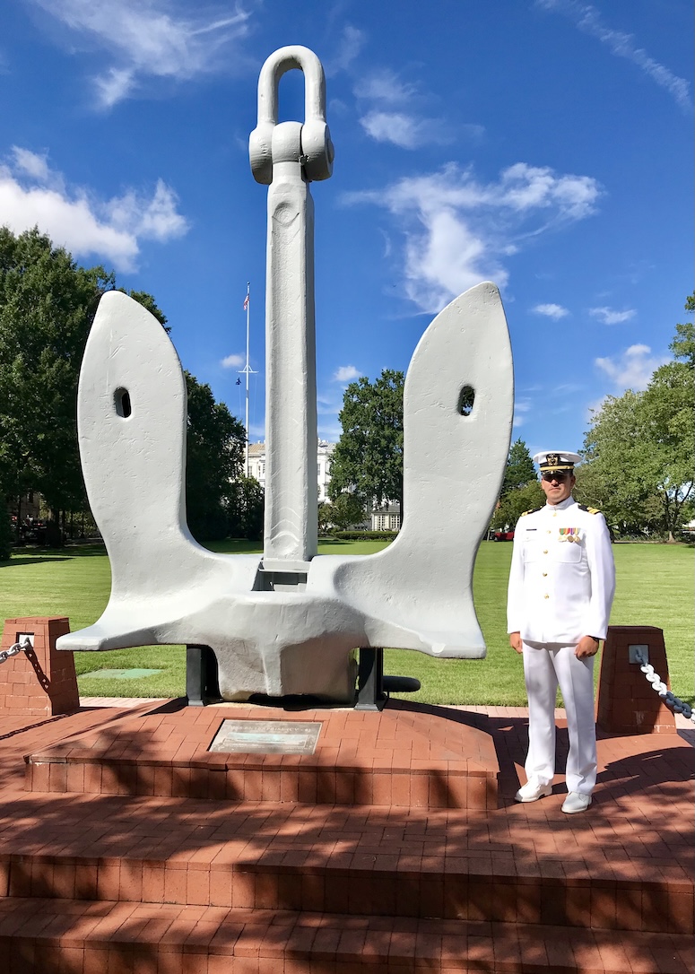 Christopher Ironroad in U.S. Navy JAG uniform standing by anchor monument, representing service to country and legal experience at Golden Grove Law PC