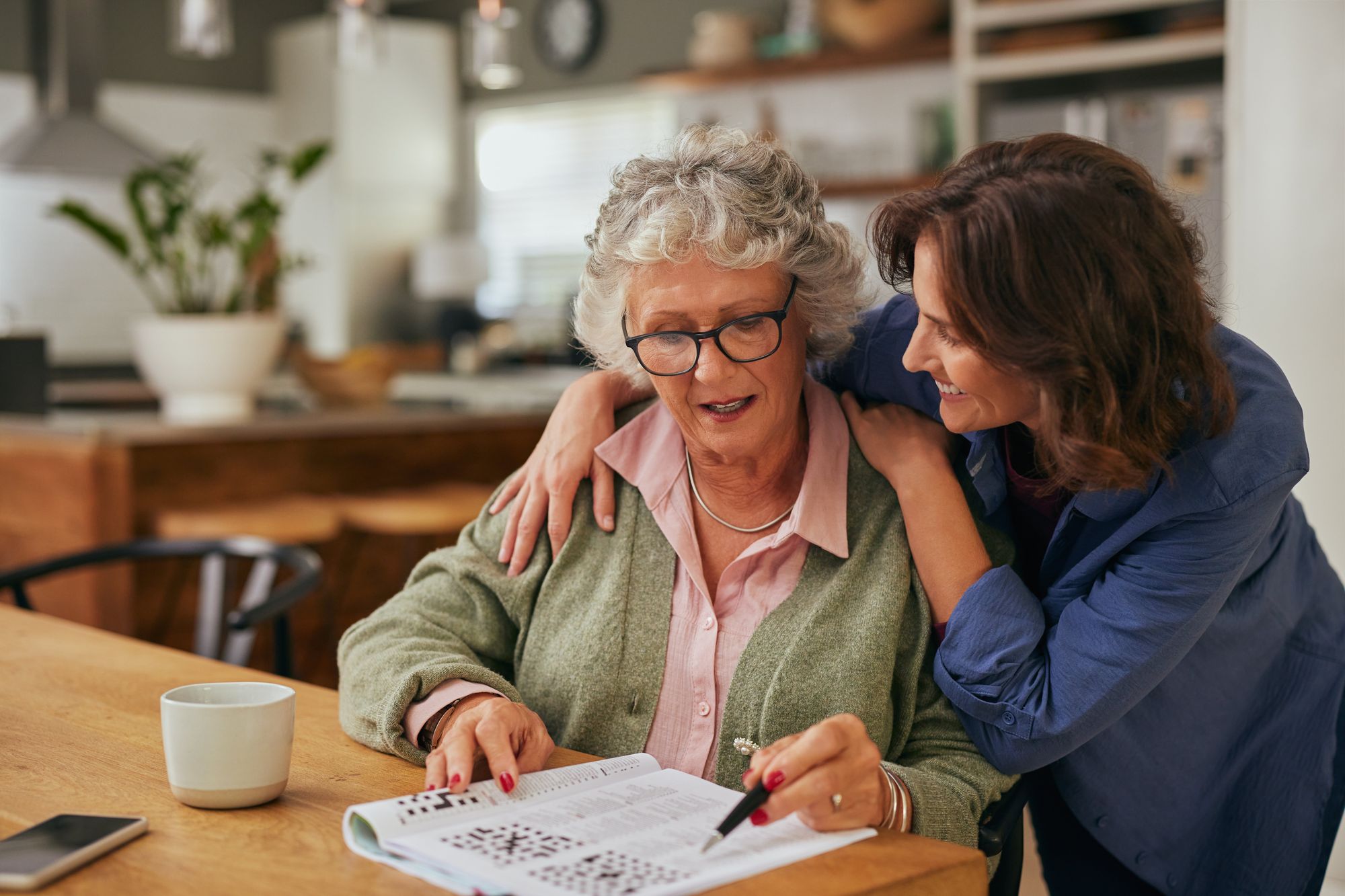 Adult daughter sitting with her senior mother at the kitchen table, working on a puzzle together