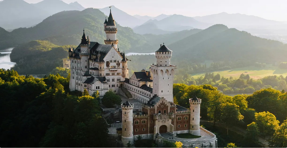 Schloss Neuschwanstein in Bayern, umgeben von Wald und Bergen bei Sonnenlicht.