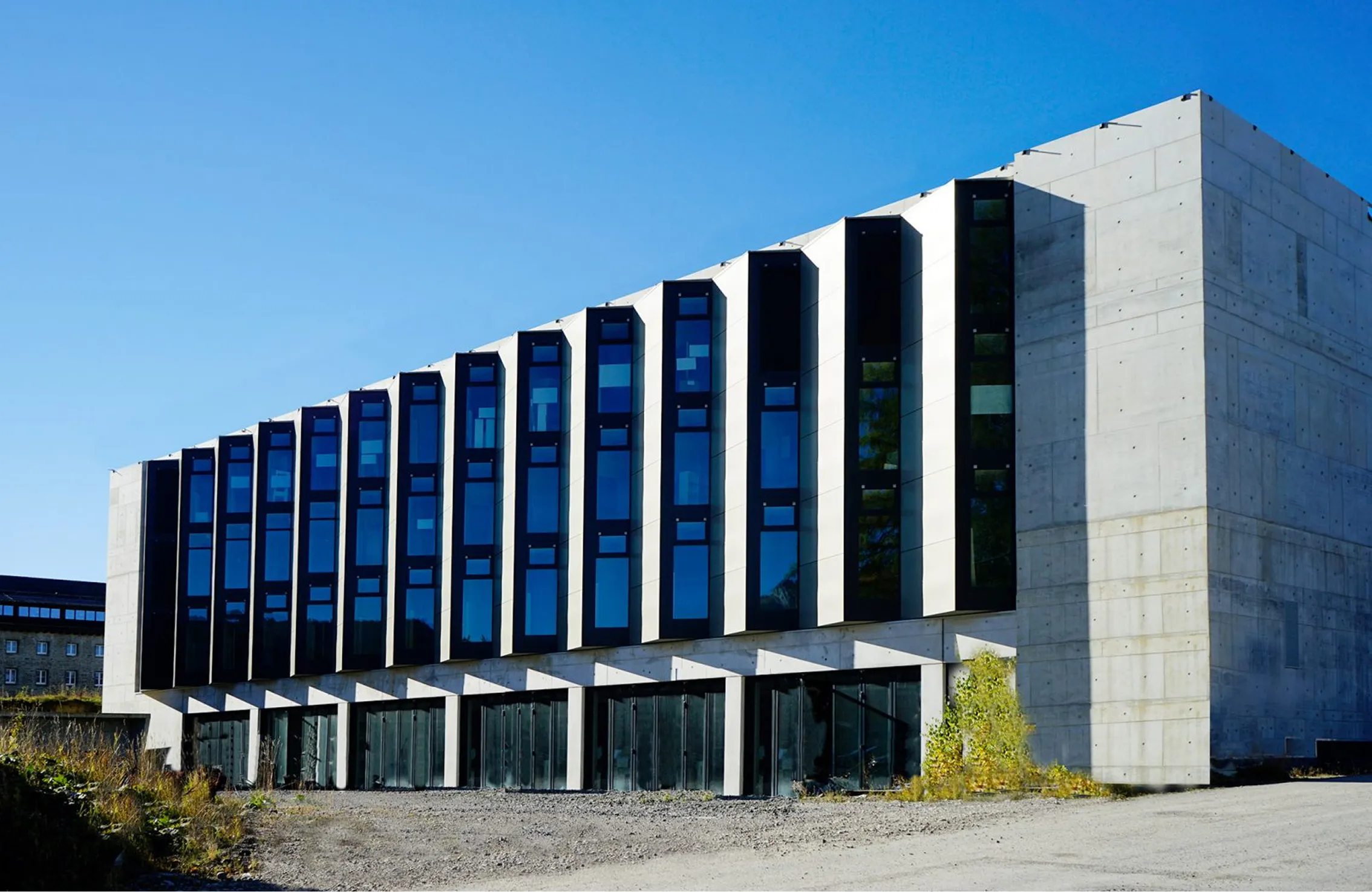 Modernes Industriegebäude mit großen vertikalen Fenstern und Betonfassade unter blauem Himmel.