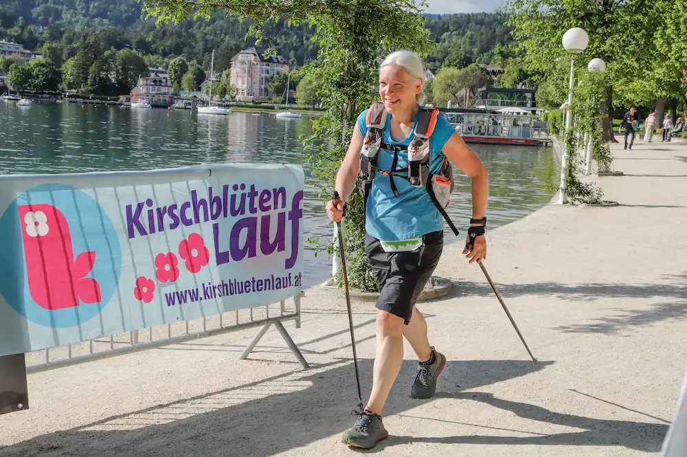 Ältere Frau mit Wanderstöcken läuft am Seeufer beim Wörthersee Trail Event