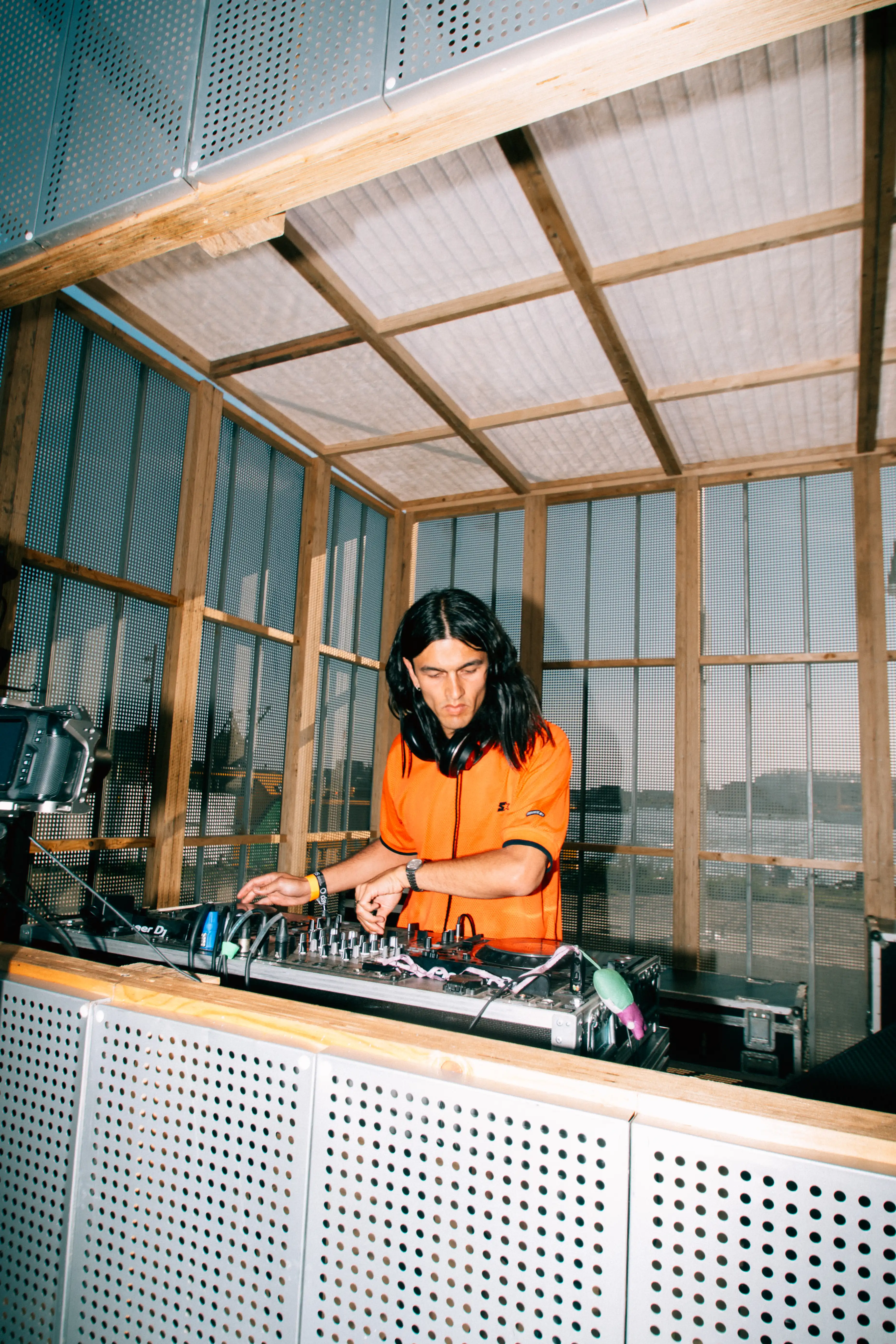 Angel Wei during his dj set at the O/FM stage during O Days, wearing an orange t-shirt and using both hands to touch the mixer.