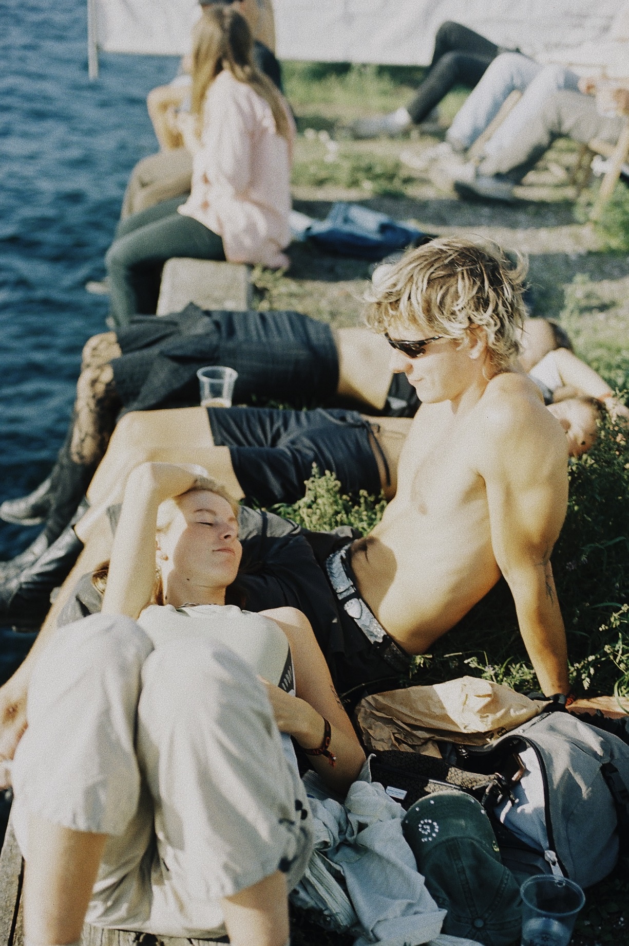 Two people sit and relax by the waterfront under the sun.