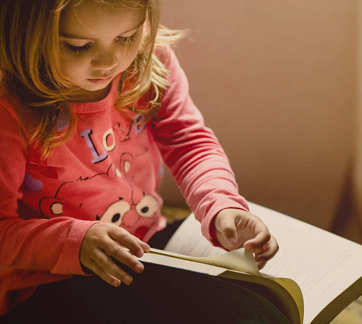 A little girl sitting down reading a book.
