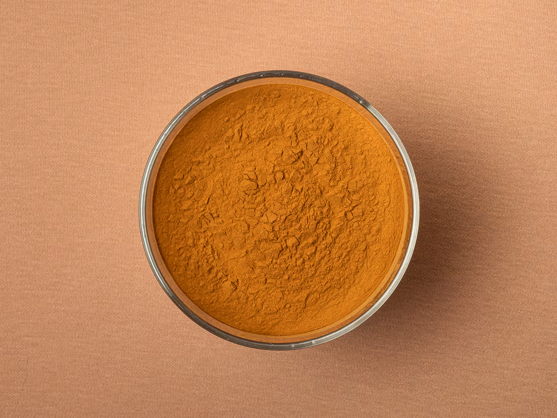 Bowl of orange pigment powder on a peach-colored textile fabric