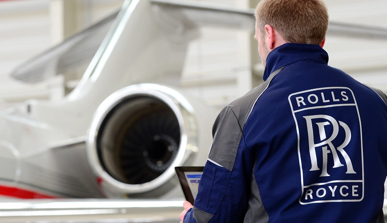 Aerospace engineer with his back to camera with the Rolls-Royce logo on his overalls and a plane in the background