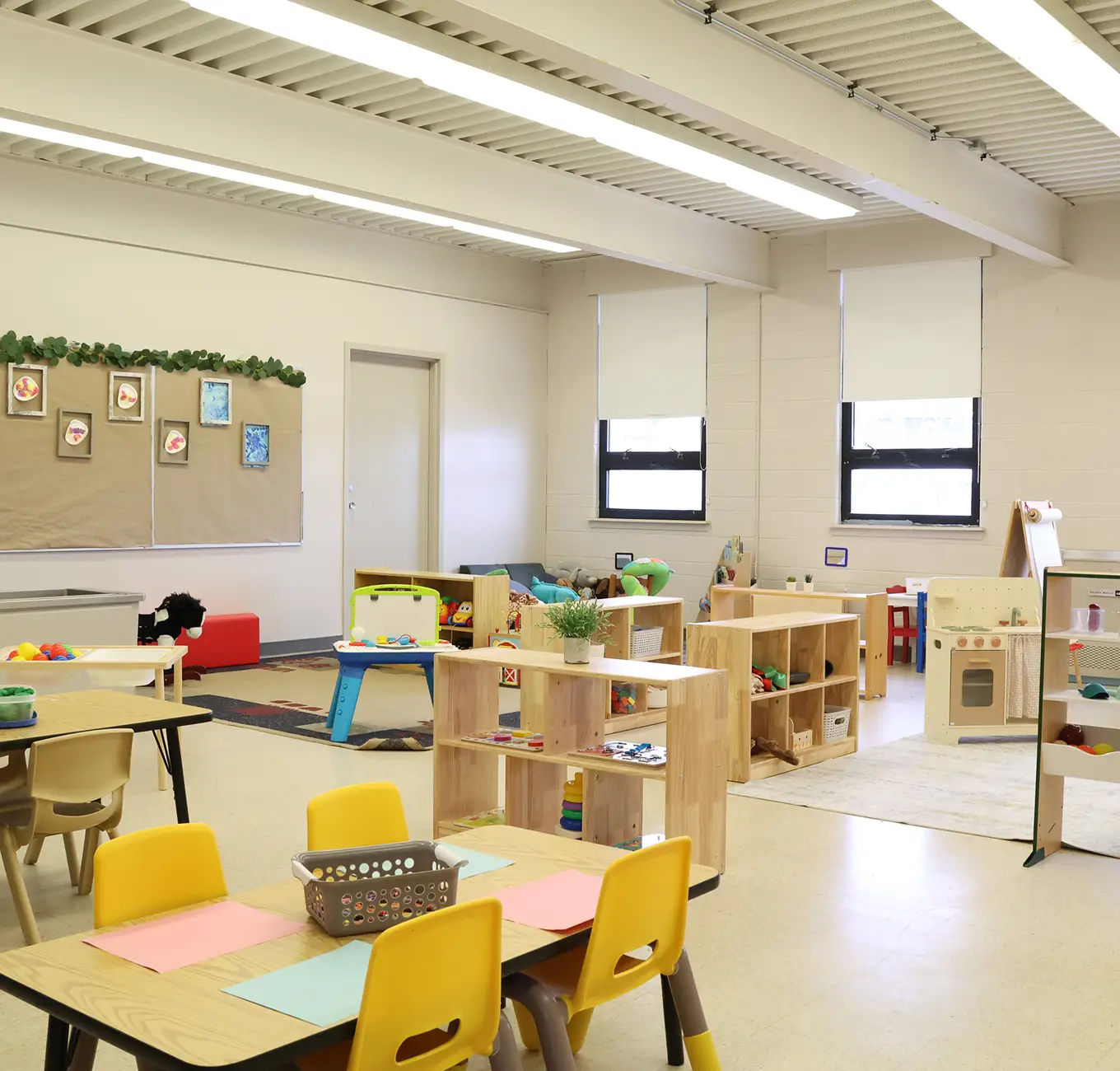 A colorful classroom with small tables, chairs, and various toys and learning materials neatly arranged.