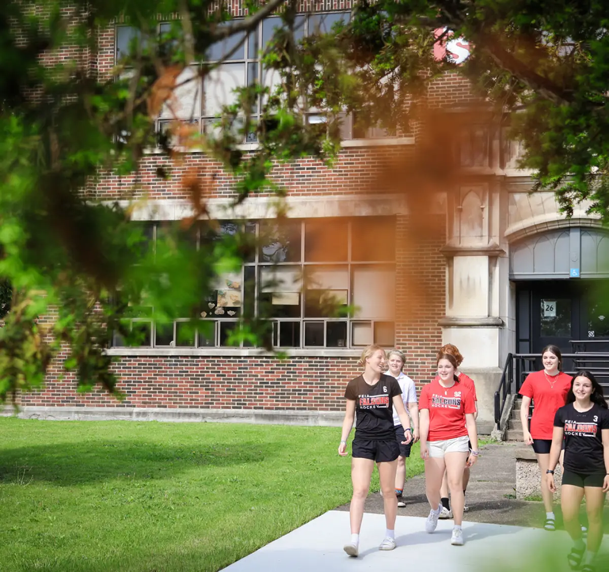A group of six people walks together on a sidewalk near a brick building.