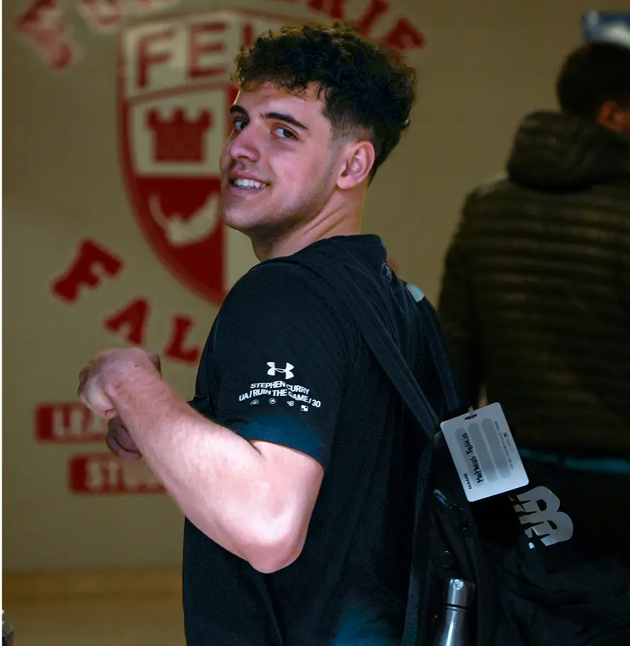 A person smiles while carrying a backpack over one shoulder inside a building.