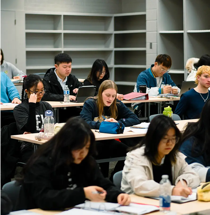 Students sitting at desks in a classroom, focused on work and writing notes.