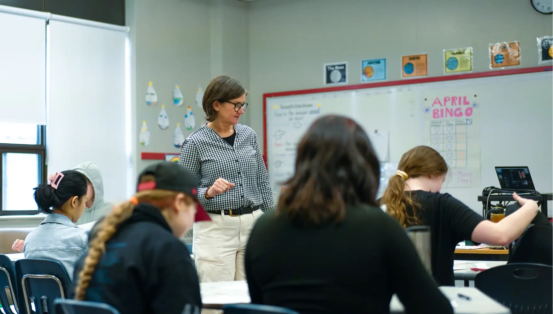 A teacher stands at the front of the classroom, talking to seated students.