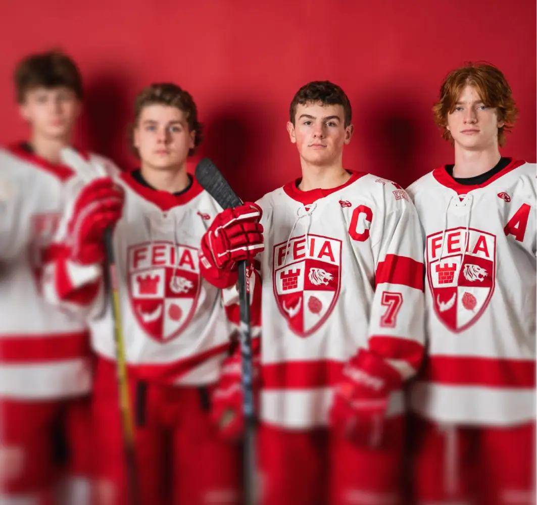 Four young hockey players in red and white uniforms stand in a line, holding sticks.
