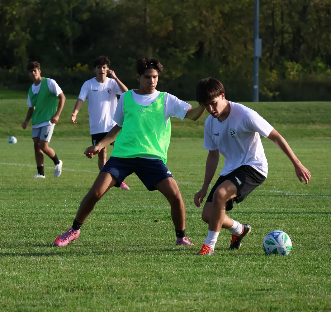 Two soccer players in practice gear compete for the ball during a training session.