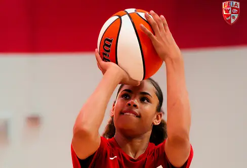 A person in a red shirt is preparing to shoot a basketball indoors.