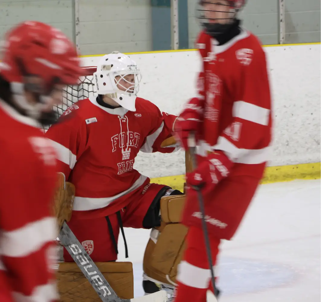 Hockey goalie in red and white gear crouches near the net during a game.
