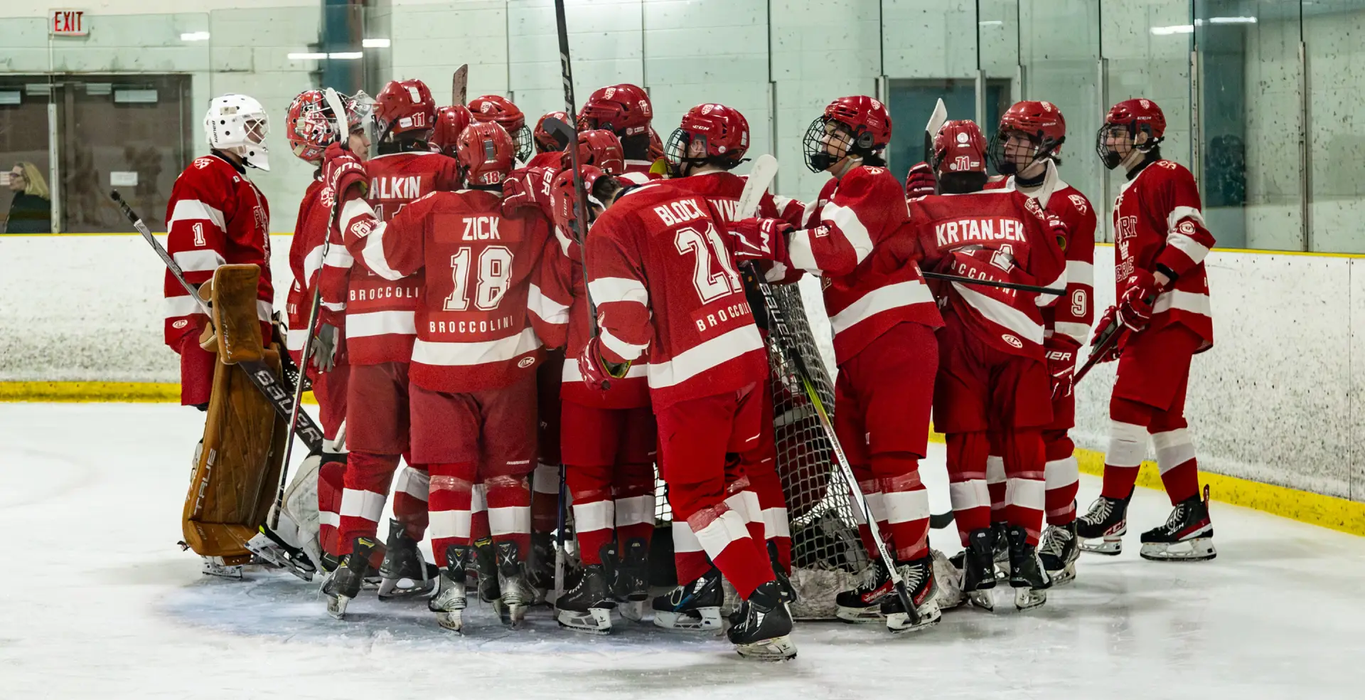 A hockey team in red uniforms huddles together on the ice rink.
