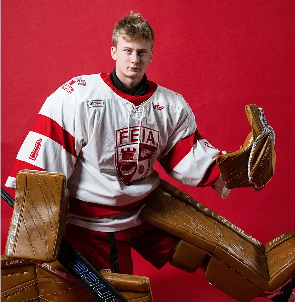 A hockey goalie in red and white gear poses with pads and glove against a red background.