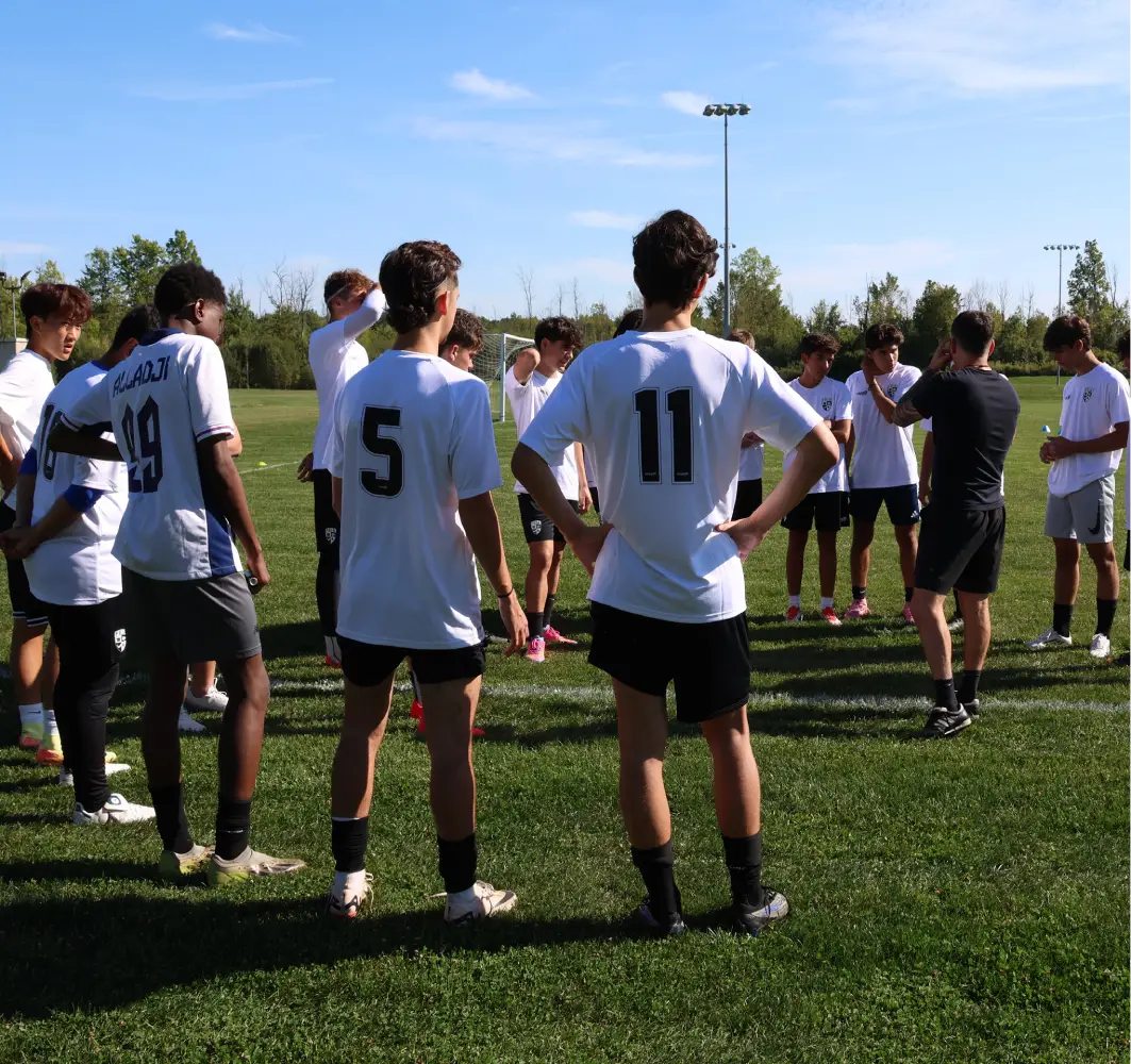 A soccer coach gives instructions to a group of players huddled on the field.