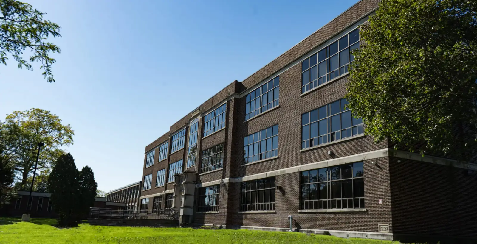 A large brick school building with numerous windows under a clear blue sky.