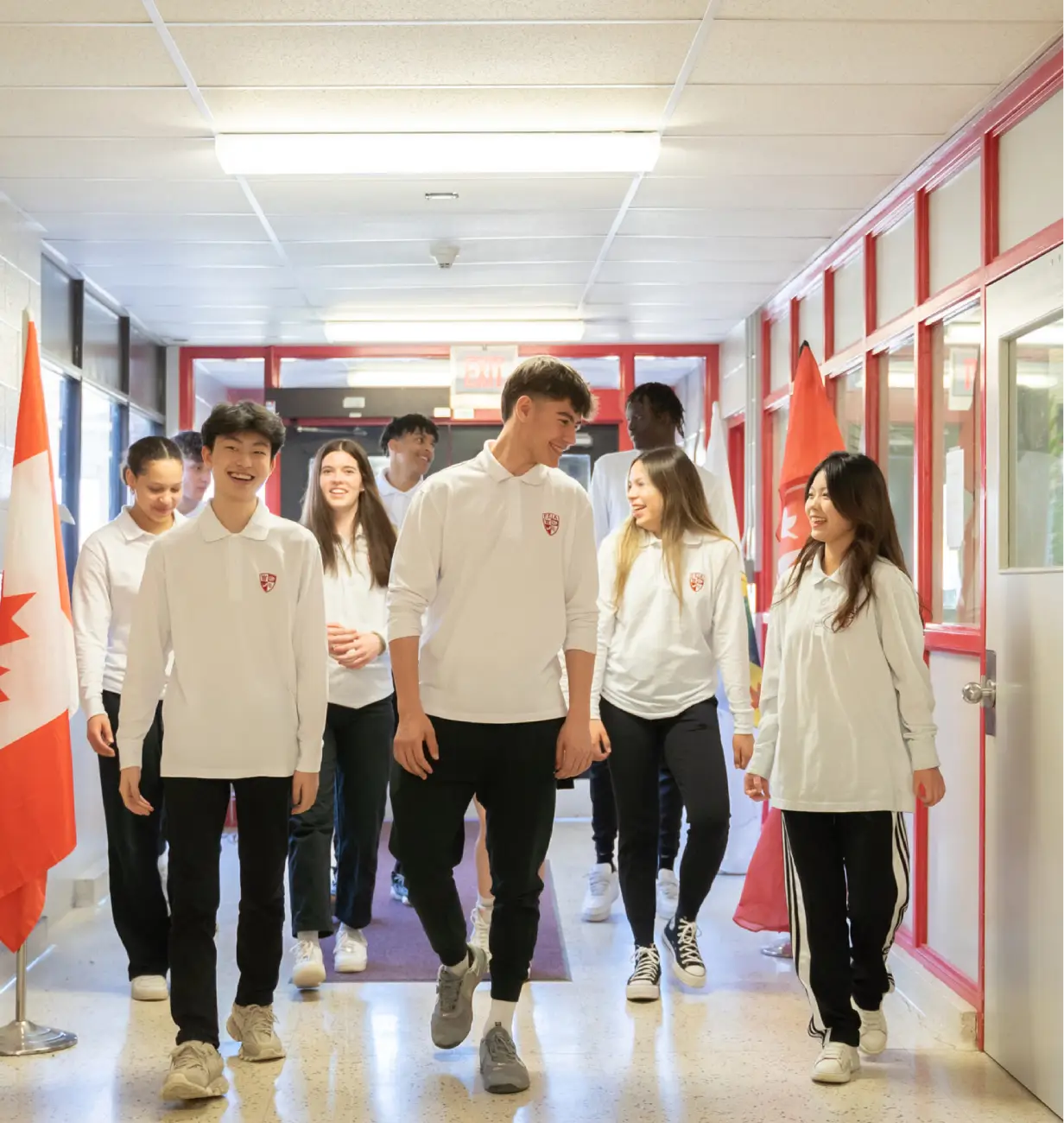 A group of students in uniforms walk together down a school hallway with flags on the side.