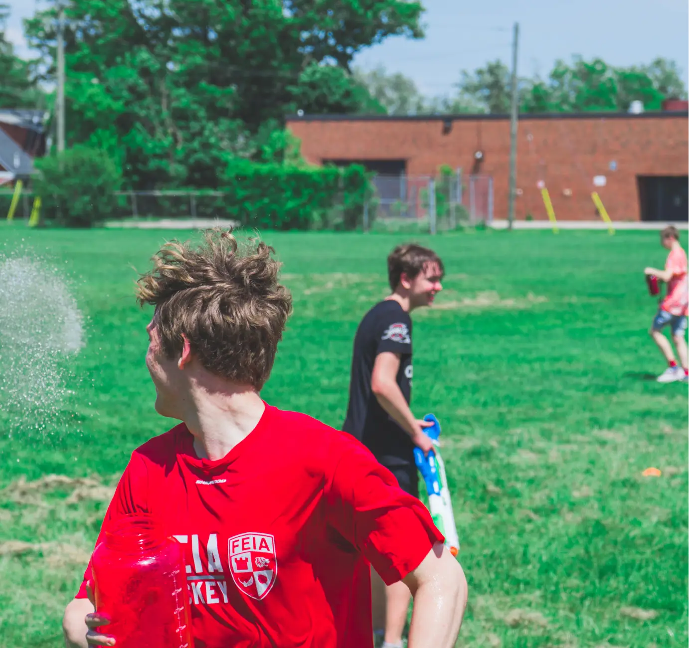 Three people playing with water guns on a grassy field, with one person holding a red water balloon.
