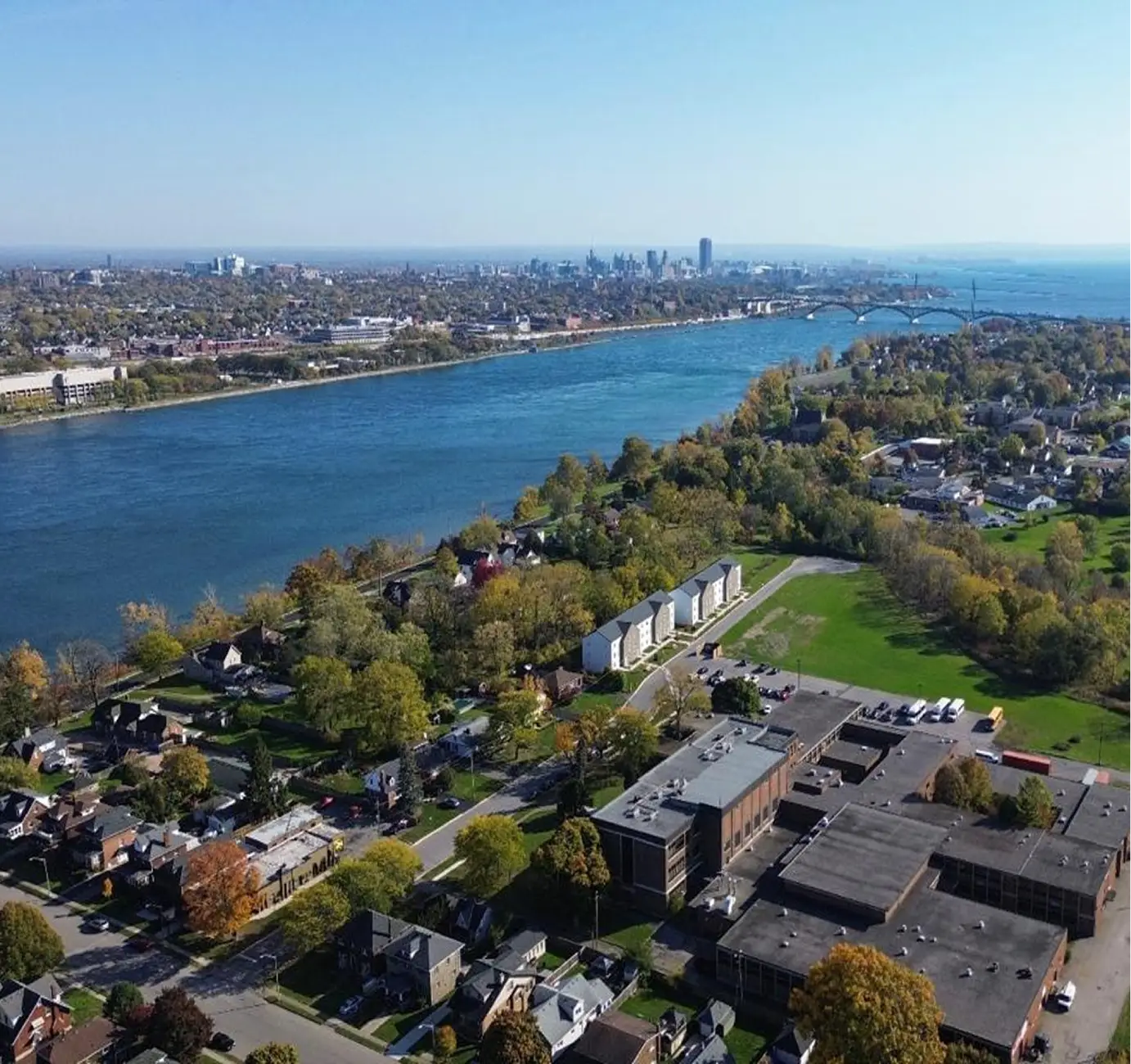Aerial view of a river with a city skyline in the background and houses along the shore.