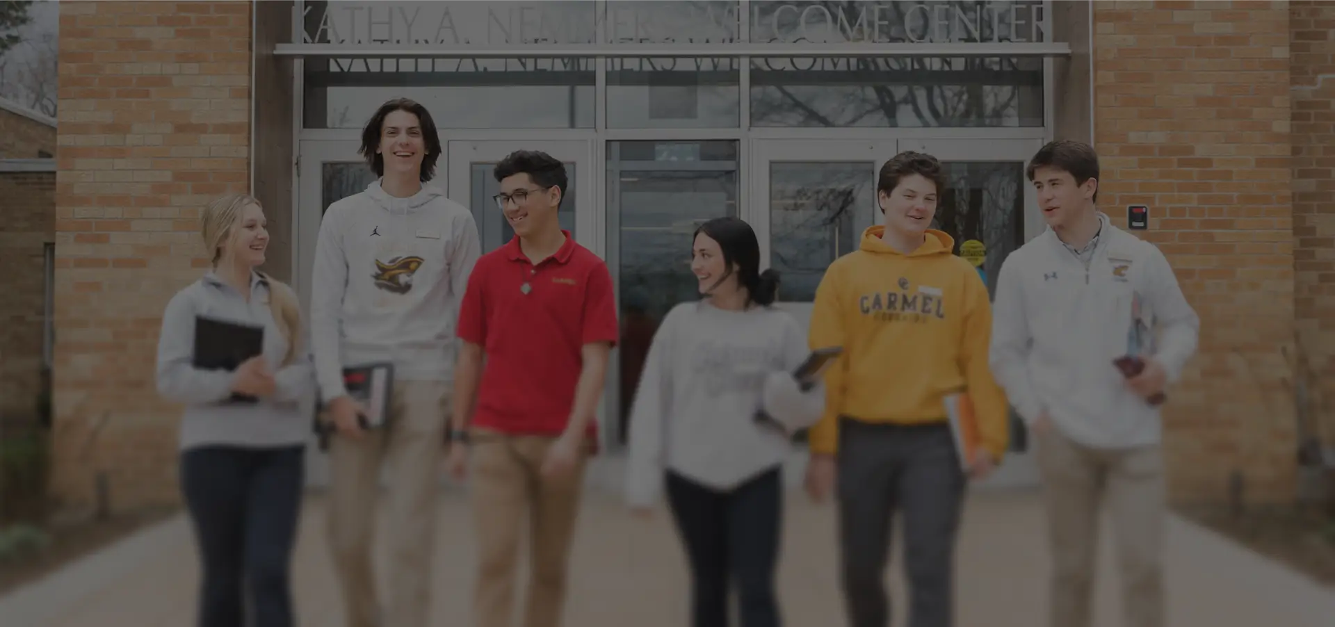 Six students walking and talking in front of a school entrance.