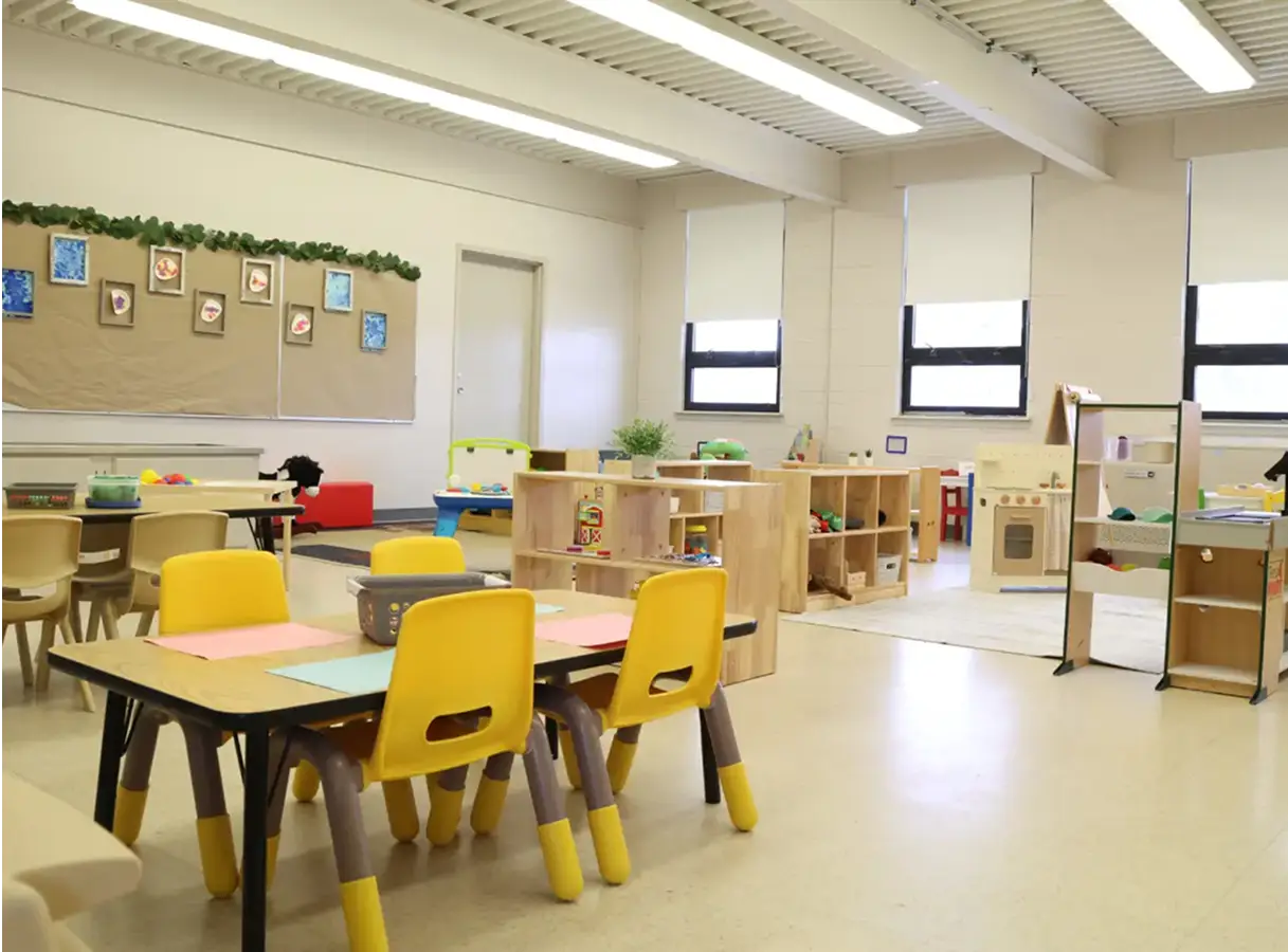 A bright classroom with small tables, chairs, and various educational toys set up for children.